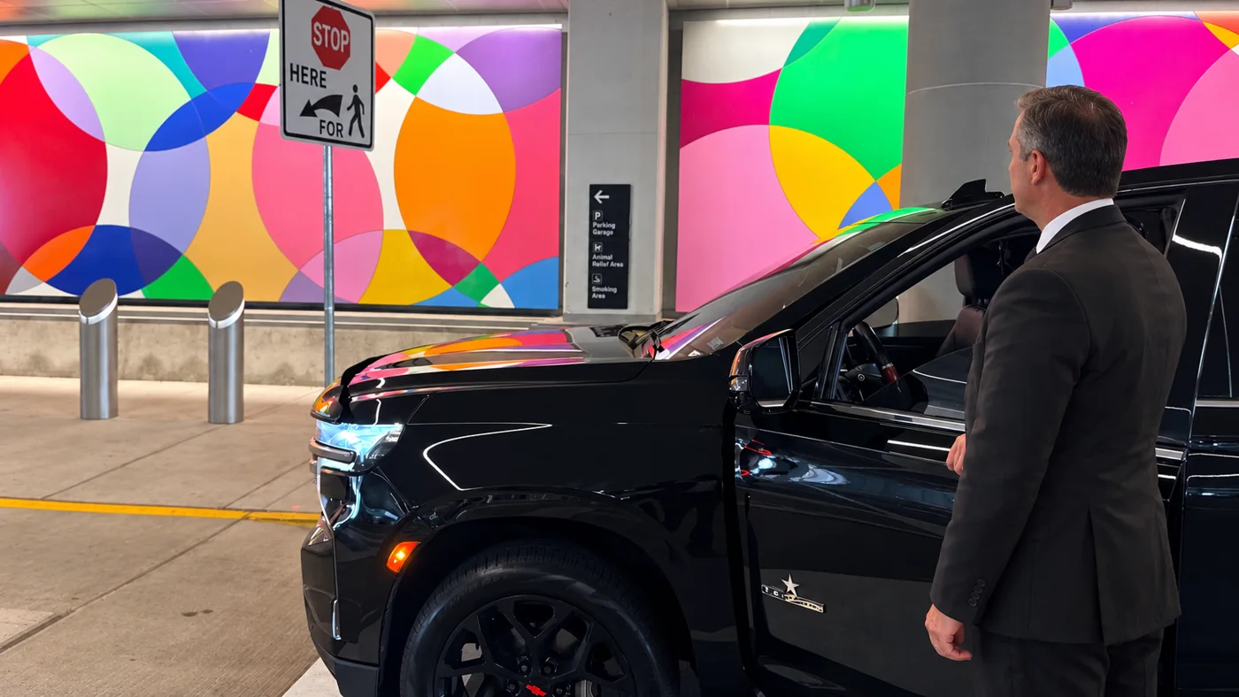 Chauffeur waiting beside a black SUV door at the IAH arrivals curb